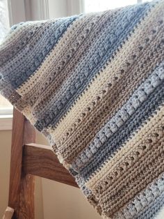 a crocheted blanket sitting on top of a wooden chair next to a window