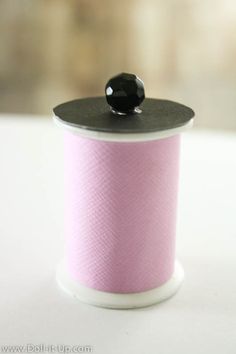 a spool of pink thread with a black button on the top is sitting on a white surface