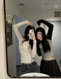 two young women taking selfies in front of a mirror with their cell phones up