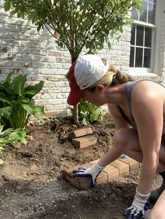 a woman kneeling down next to a tree in the dirt with gardening gloves on her feet