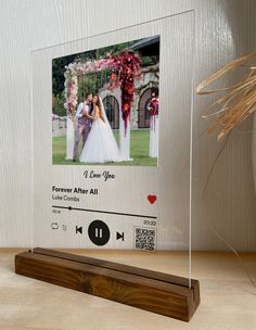 a clear acrylic photo frame with a wooden stand on a table next to a vase