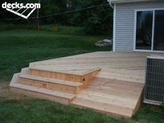 a wooden deck in front of a house with an air conditioner on the side