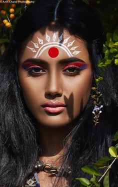 a woman with makeup painted on her face and head is surrounded by greenery as she poses for the camera