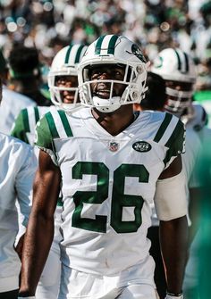 a football player wearing a green and white uniform is walking on the field with other players in the background