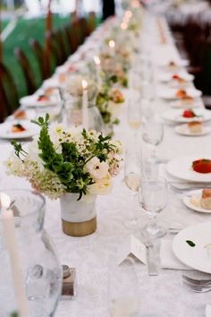 a long table is set up with white plates and silverware, candles and flowers in vases