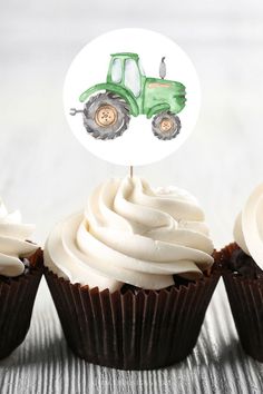 three cupcakes with white frosting and a green tractor sticker on top