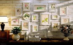 there are many frames on the wall with flowers and plants in them next to a lamp