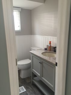 a white toilet sitting next to a bathroom sink under a window in a room with gray walls