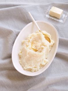 mashed potatoes and butter in a white bowl with two spoons on the side