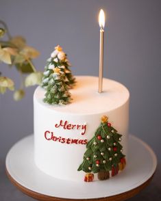 a white christmas cake with two small trees on it and a lit candle in the middle