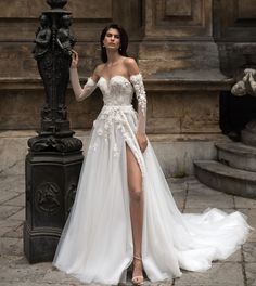 a woman standing next to a lamp post wearing a dress with long sleeves and high slit