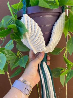 a hand holding a potted plant with white and green yarn hanging from it's side