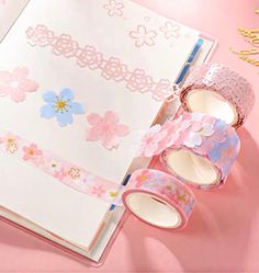 an open book with pink and blue flowers on it next to some washi tape