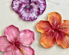 three different colored flowers sitting on top of a white countertop next to each other