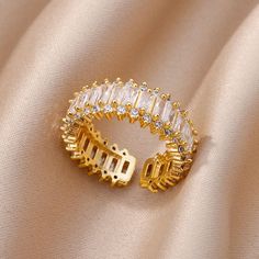 a gold ring with white stones on it sitting on top of a satin material background