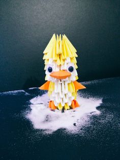 an origami bird sitting on top of some white powdered paper and looking at the camera