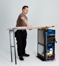 a man standing next to a table with tools in it and holding a piece of wood