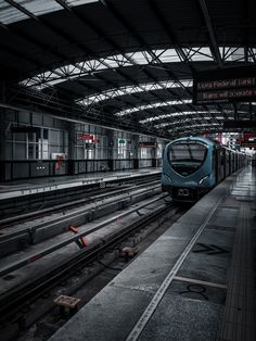 a blue train traveling down tracks next to a loading platform at a train station in the dark