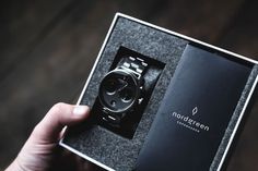 a person holding up a watch in a black box with the word norddsteen written on it