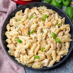 a bowl filled with pasta and chicken on top of a table next to basil leaves