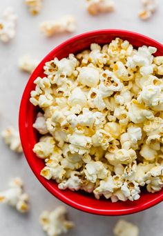 a red bowl filled with popcorn sitting on top of a white tablecloth covered floor