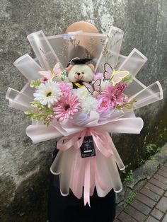 a teddy bear sitting on top of a vase filled with pink flowers and daisies