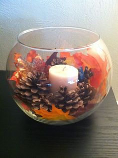 a glass bowl filled with pine cones and a lit candle