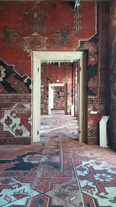 an ornate hallway with red walls and rugs on the floor, leading to two doors