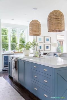 a large kitchen with blue cabinets and white counter tops, two hanging lamps above the island