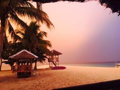 the beach is lined with palm trees and thatched umbrellas, while the sun sets