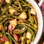 green beans and potatoes in a white bowl on a wooden table with red checkered napkins