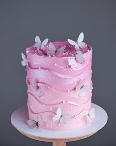 a pink cake with butterflies on it sitting on top of a wooden table in front of a gray wall