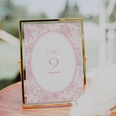 the table numbers are displayed in pink and gold frames on top of a wooden table