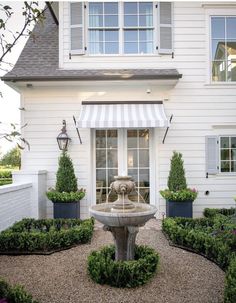 a white house with a fountain in front of it and bushes around the outside area