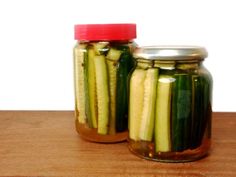 two jars filled with pickles sitting on top of a wooden table