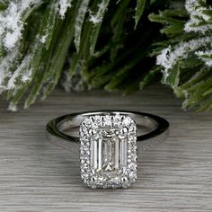 an emerald - cut diamond ring sits on a table next to snow covered evergreen branches