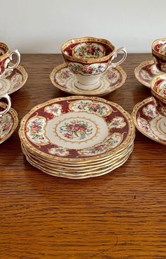 a wooden table topped with lots of fancy plates and cups on top of each other