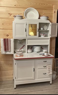 a white kitchen cabinet with red trim and plates on the top, in front of a wood paneled wall