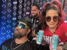 two men and a woman holding up cans of energy drink in front of a backdrop