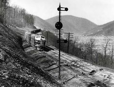 black and white photograph of a train coming down the tracks in front of some mountains