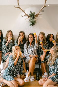 a group of women sitting next to each other holding drinks in their hands and wearing plaid shirts