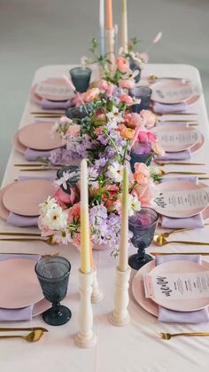 the table is set with pink and purple plates, silverware, candles, and floral centerpieces