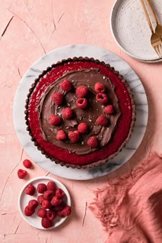 a chocolate and raspberry tart on a white plate next to a bowl of raspberries