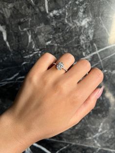 a woman's hand with a diamond ring on her left hand, against a marble background