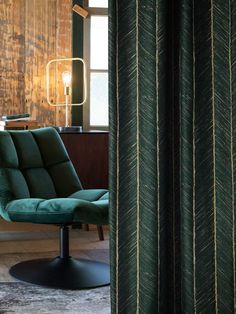 a green chair sitting in front of a window next to a wooden table with a lamp on it