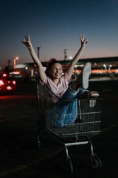 a woman sitting in a shopping cart with her arms up