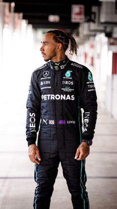 a man with dreadlocks standing in front of a building wearing a racing suit