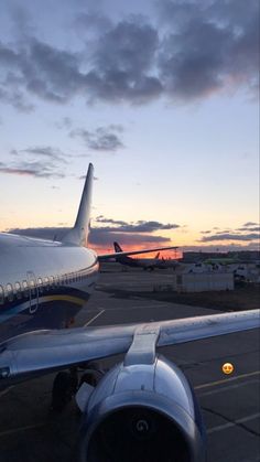 an airplane sitting on the tarmac at dusk with clouds in the sky behind it