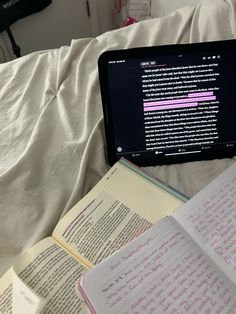 an open laptop computer sitting on top of a bed next to notebooks and books