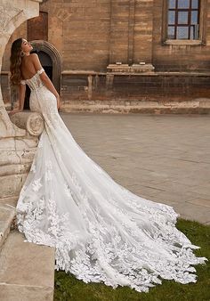 a woman in a wedding dress leaning against a stone wall with her back to the camera